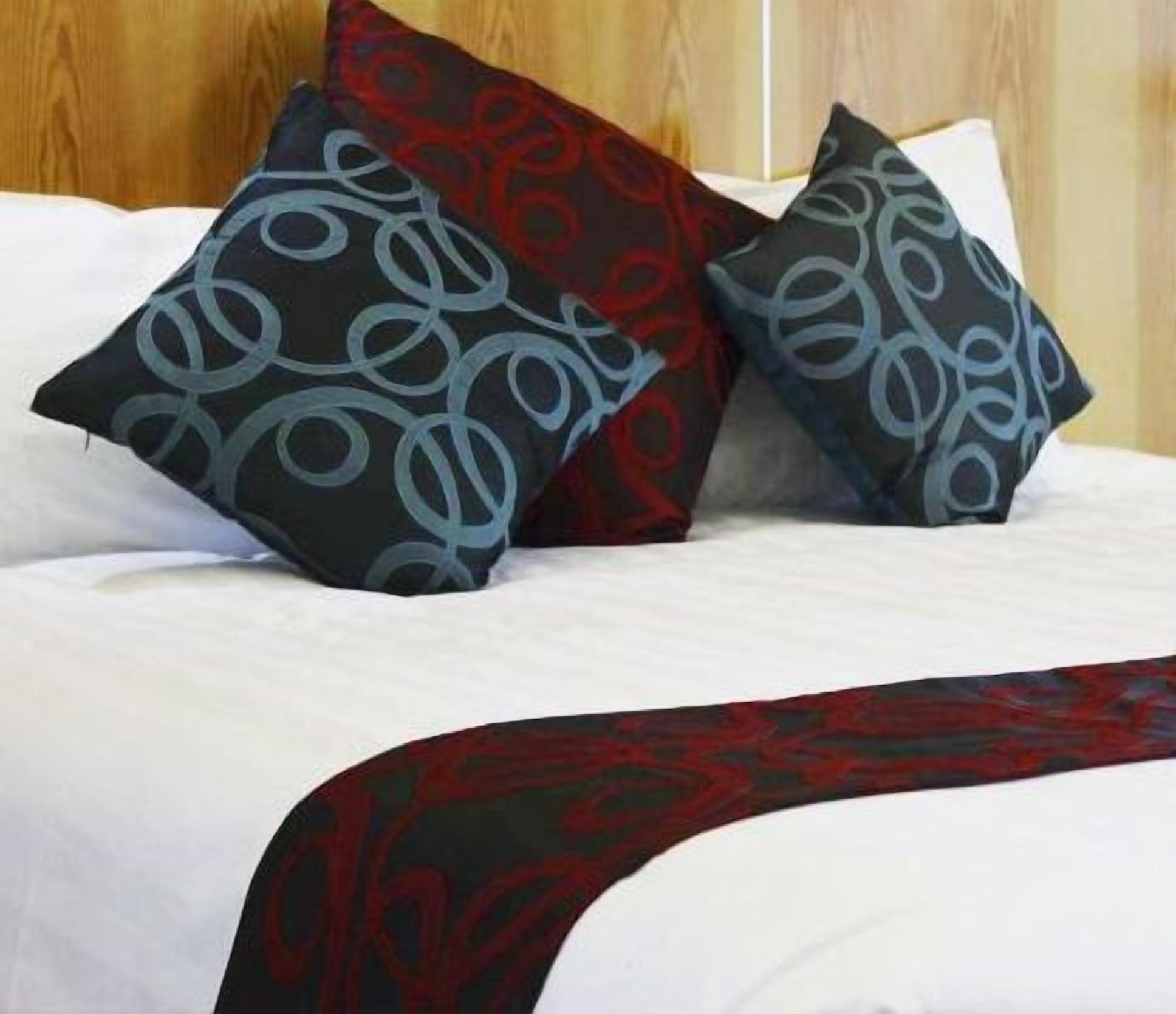 Ein Bett mit zwei gemusterten Kissen und einer dunkelroten und schwarzen Tagesdecke.