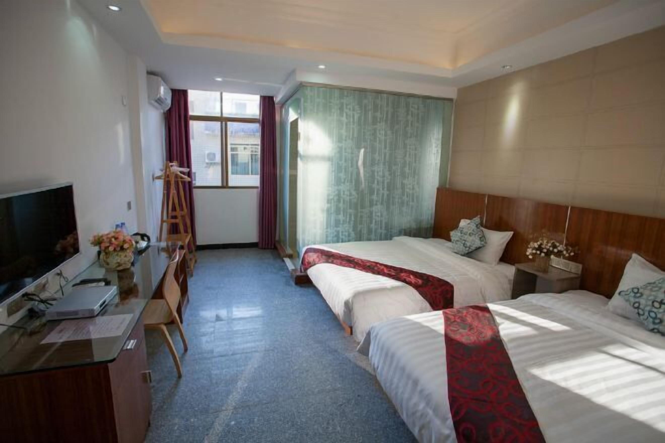 A hotel room with two beds, a desk with a computer, a TV, and a window with curtains.