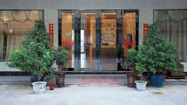A hotel entrance with glass doors, potted plants, and red banners. - Starry Inn (Renhua)
