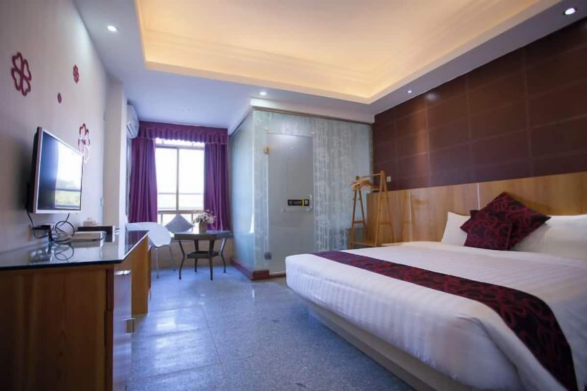 A hotel room with a bed, desk, TV, and a bathroom with a shower.