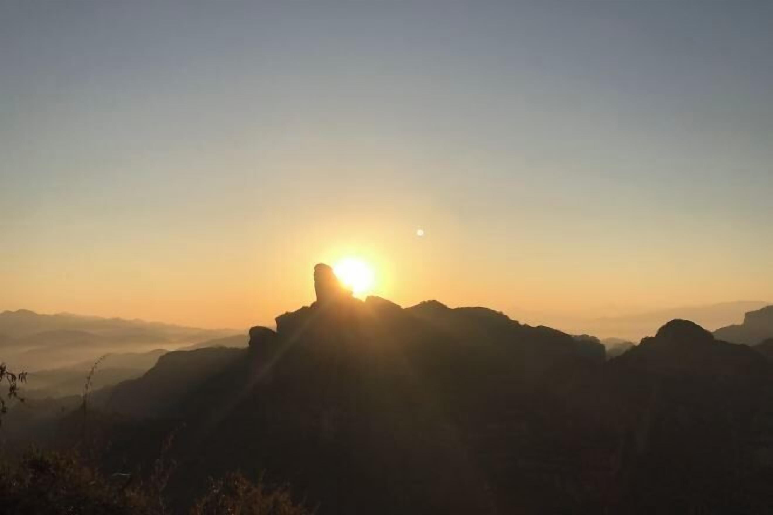 A mountain landscape with the sun setting behind the peaks.