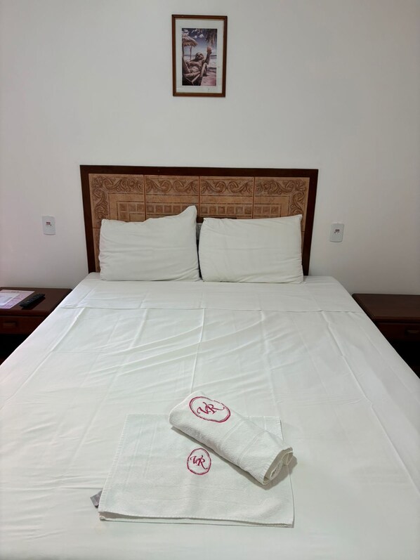 A neatly made bed with white linens and two pillows, a wooden headboard with a decorative pattern, and a framed picture on the wall above. - Pousada Villa Rosada (Santa Cruz Cabralia)