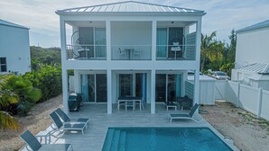 Ein zweistöckiges Haus mit Pool, Außenmöbeln und einer überdachten Terrasse.