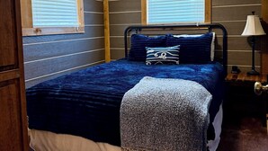 A bedroom with a bed, two windows, a ceiling fan, and a nightstand with a lamp. - Captains Cottage is the perfect retreat (Afton)