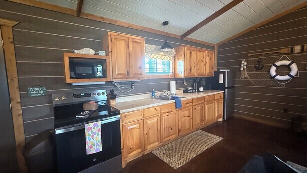 A kitchen with wooden cabinets, a microwave, a stove, and a refrigerator. - Captains Cottage is the perfect retreat (Afton)