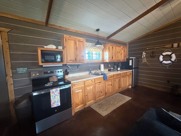 A kitchen with wooden cabinets, a microwave, a stove, and a refrigerator. - Captains Cottage is the perfect retreat (Afton)