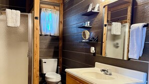 A bathroom with wooden walls, a white sink, and a mirror. There are towels hanging on the wall and a shower curtain. - Captains Cottage is the perfect retreat (Afton)