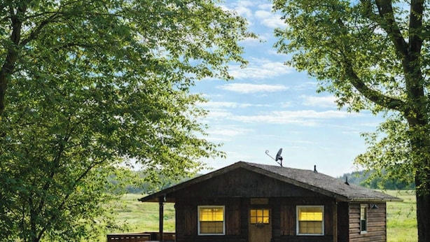 A rustic cabin with a sloped roof, two windows with yellow curtains, and a satellite dish on the roof. - Knots Landing - A romantic getaway w/ hot tub (Afton)