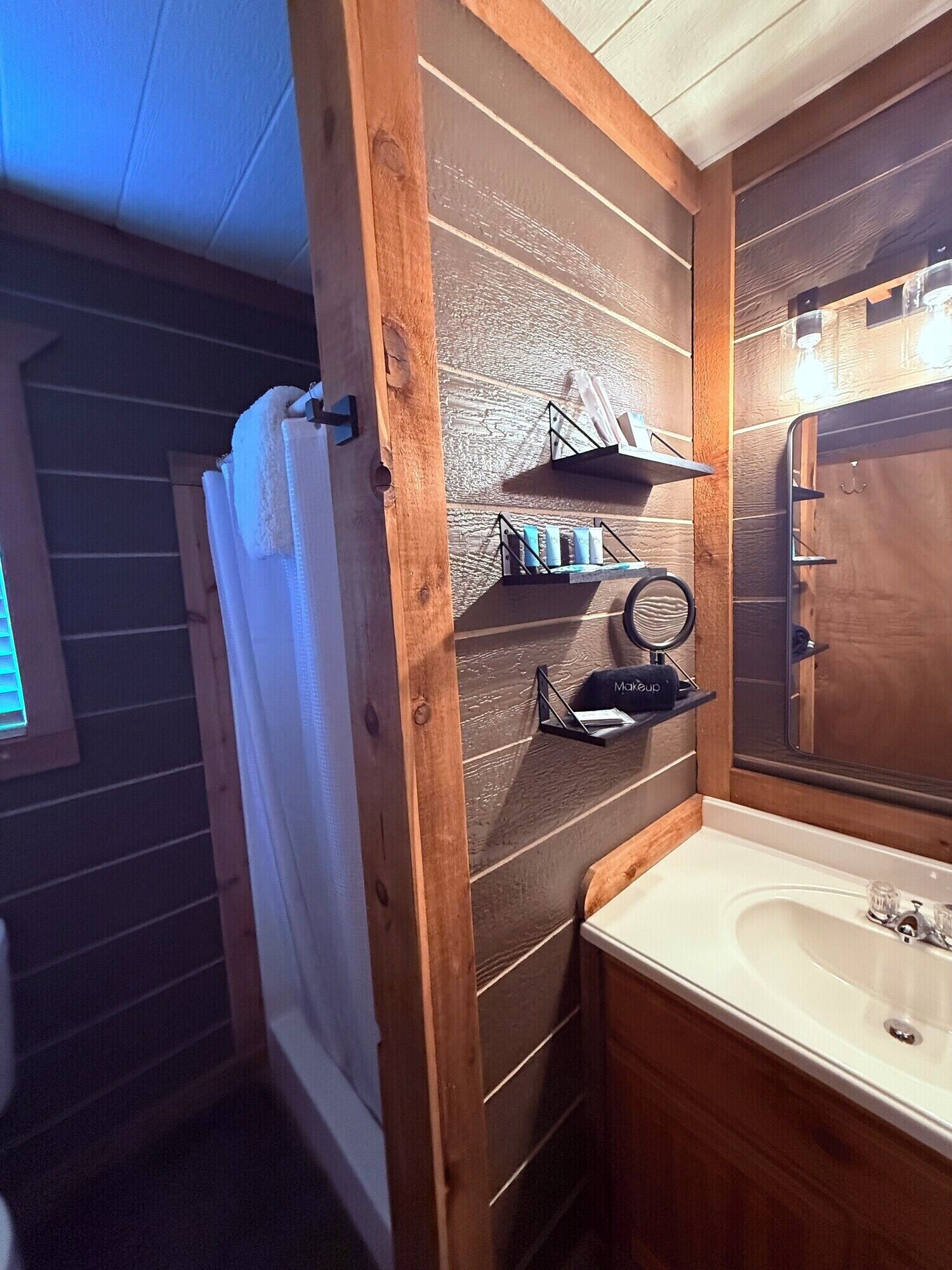 Une salle de bain avec un meuble-lavabo en bois, un miroir et une étagère contenant des articles de toilette.