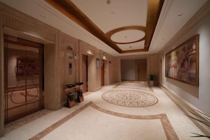 Corredor de hotel com piso estampado, teto com design circular e um quadro na parede.
