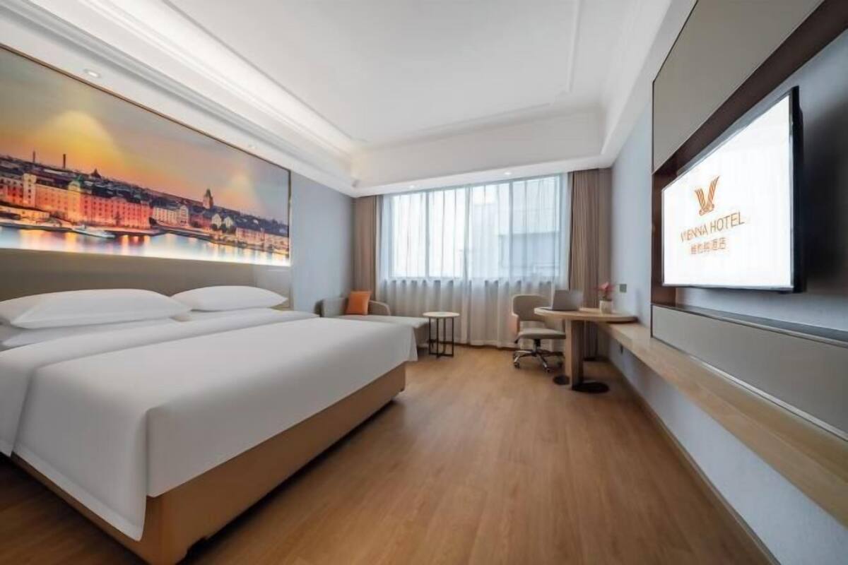 Una habitación de hotel con una cama grande, un escritorio, una silla y un televisor montado en la pared.