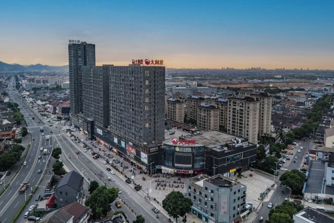 Un edificio alto con varios pisos, rodeado por una concurrida calle urbana con coches y peatones.
