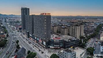 Un edificio alto con varios pisos, rodeado por una concurrida calle urbana con coches y peatones.