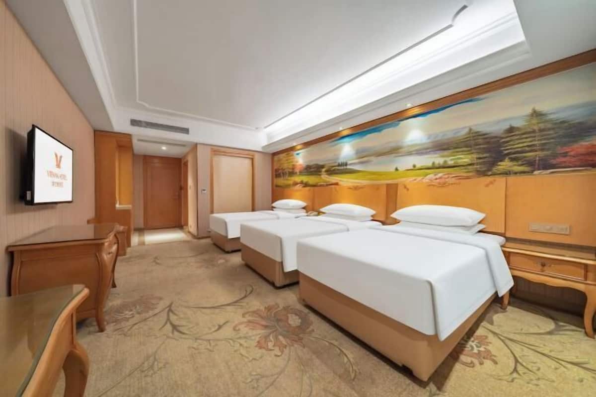 Habitación de hotel con tres camas, un escritorio y una televisión.