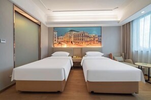 Une chambre d’hôtel avec deux lits simples, un tableau représentant un paysage urbain accroché au mur, une petite table et une chaise.