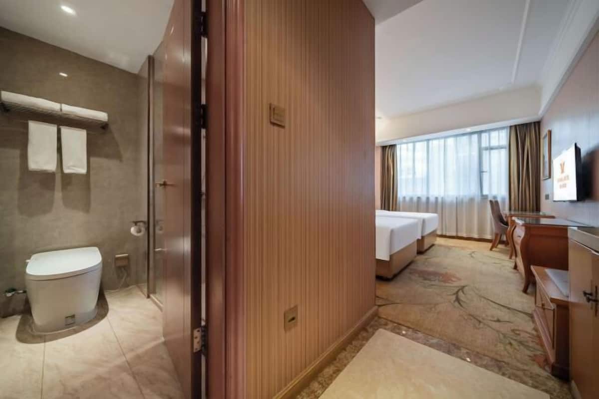 Habitación de hotel con baño, cama, escritorio y un amplio ventanal.