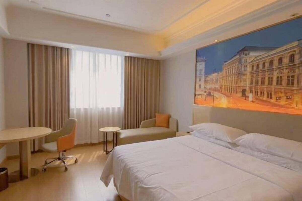 Habitación de hotel con una cama grande, un escritorio, una silla y una pequeña mesa. En la pared, un cuadro que representa una escena callejera.
