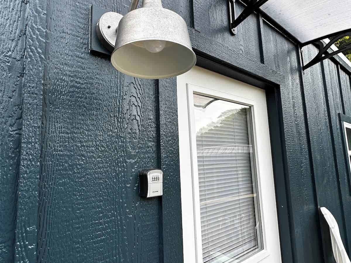 Et hus med en hvid dør, et vindue med rullegardiner, en vægmonteret lampe og en sikkerhedstastatur.