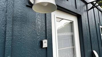 Et hus med en hvid dør, et vindue med rullegardiner, en vægmonteret lampe og en sikkerhedstastatur.