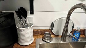 Et køkkenområde med en stålvask, en hvid kop med teksten 'chef's tools', en sort taske og en flaske Dawn opvaskesæbe.