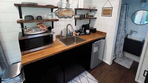 Et kompakt køkken med træbordplade, indbygget ovn, vask og kaffestation.