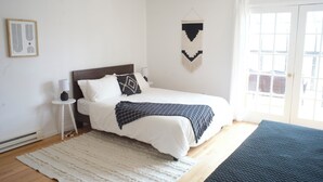 Ein Schlafzimmer mit einem Bett, einem Nachttisch, einer Wandweberei und einem großen Fenster.