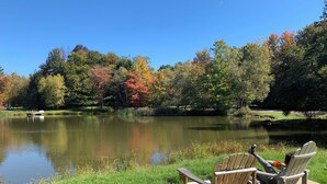 Eine Holzterrasse mit Adirondack-Stühlen mit Blick auf einen stillen See, umgeben von Bäumen mit Herbstlaub.