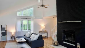 Ein modernes Wohnzimmer mit Kamin in Schwarz, Deckenventilator und großem Fenster für natürliches Licht.