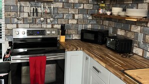 A kitchen with a brick backsplash, stainless steel appliances, wooden countertops, and white cabinets. - Rio Verde - Cozy Cottage on the Frio River  (Leakey)