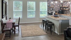 A spacious kitchen with a large island, wooden bar stools, and a dining area with a table and chairs. - Rio Verde - Cozy Cottage on the Frio River  (Leakey)