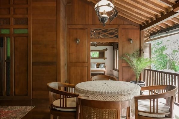 A wooden interior with a round table and chairs, a hanging light fixture, and a view of the outdoors. - The Lavana Ziza Living And Villas Seminyak (Bali)