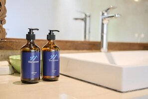Two amber bottles with pump dispensers on a bathroom counter, a white sink, and a mirror in the background. - The Lavana Ziza Living And Villas Seminyak (Bali)