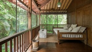 A wooden deck with a sofa and a small table, surrounded by lush greenery. - The Lavana Ziza Living And Villas Seminyak (Bali)
