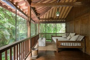 A wooden deck with a sofa and a small table, surrounded by lush greenery.