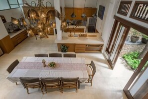 A modern kitchen with a dining area, featuring a long table with chairs, a chandelier, and a view of the outdoors. - The Lavana Ziza Living And Villas Seminyak (Bali)