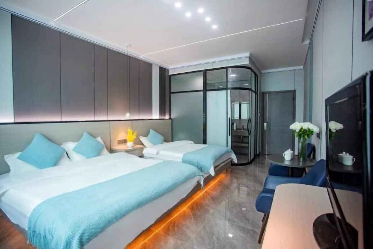 A modern hotel room with two beds, a dining table, and a TV.