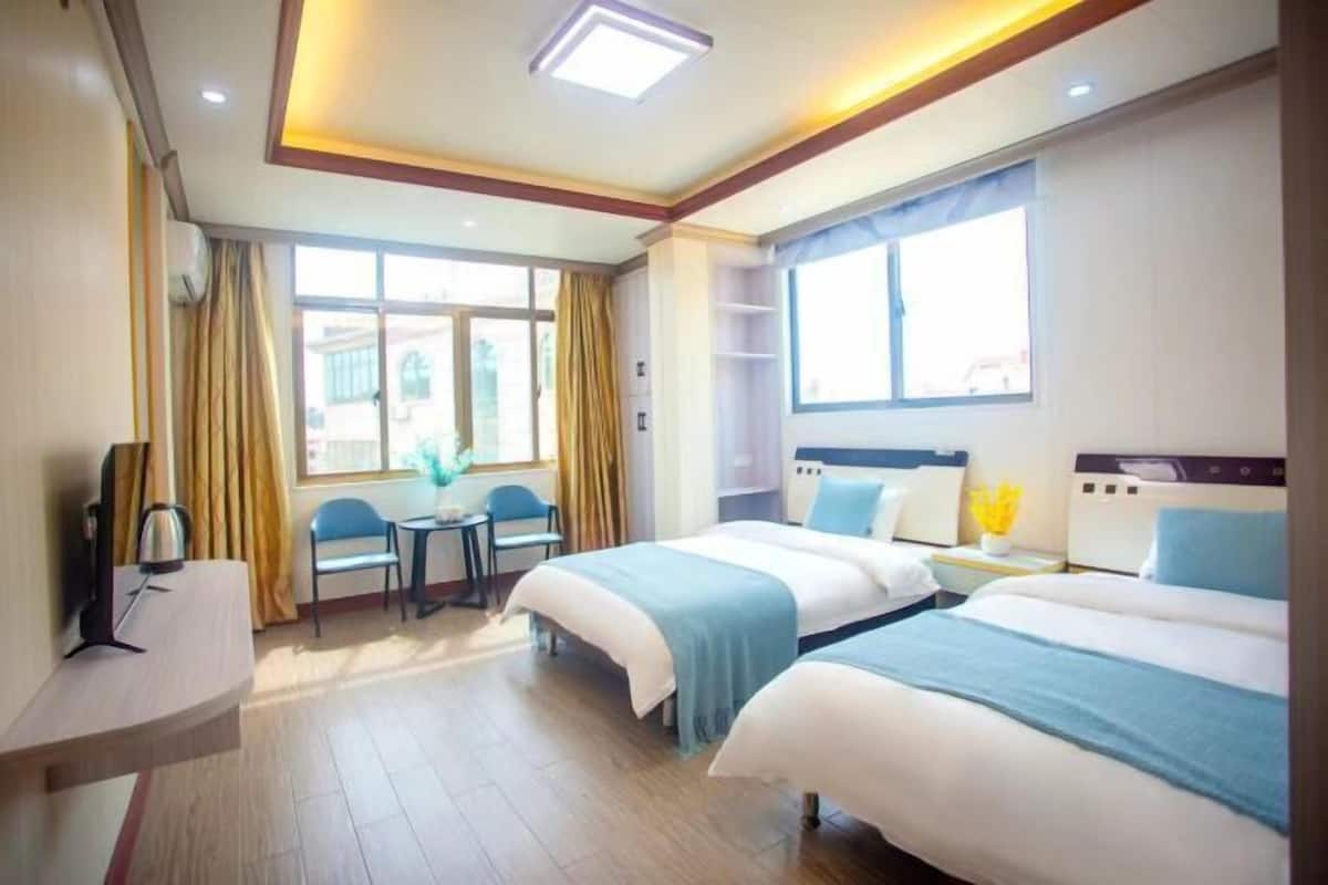 A hotel room with two beds, a desk, a chair, and a window with curtains.