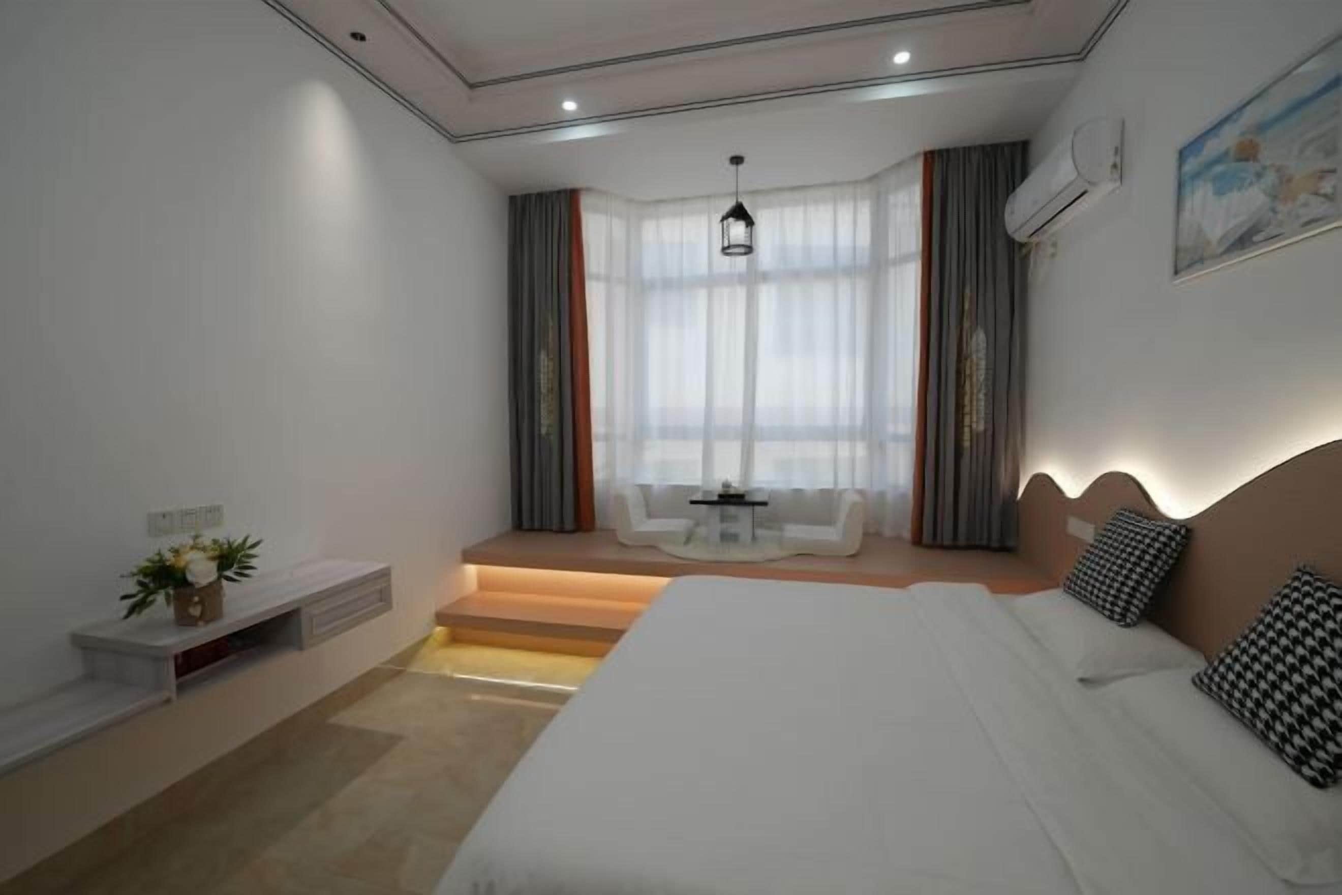 Une chambre d’hôtel moderne dotée d’un grand lit, d’un petit coin salon avec une table et offrant une vue à travers des rideaux légers.