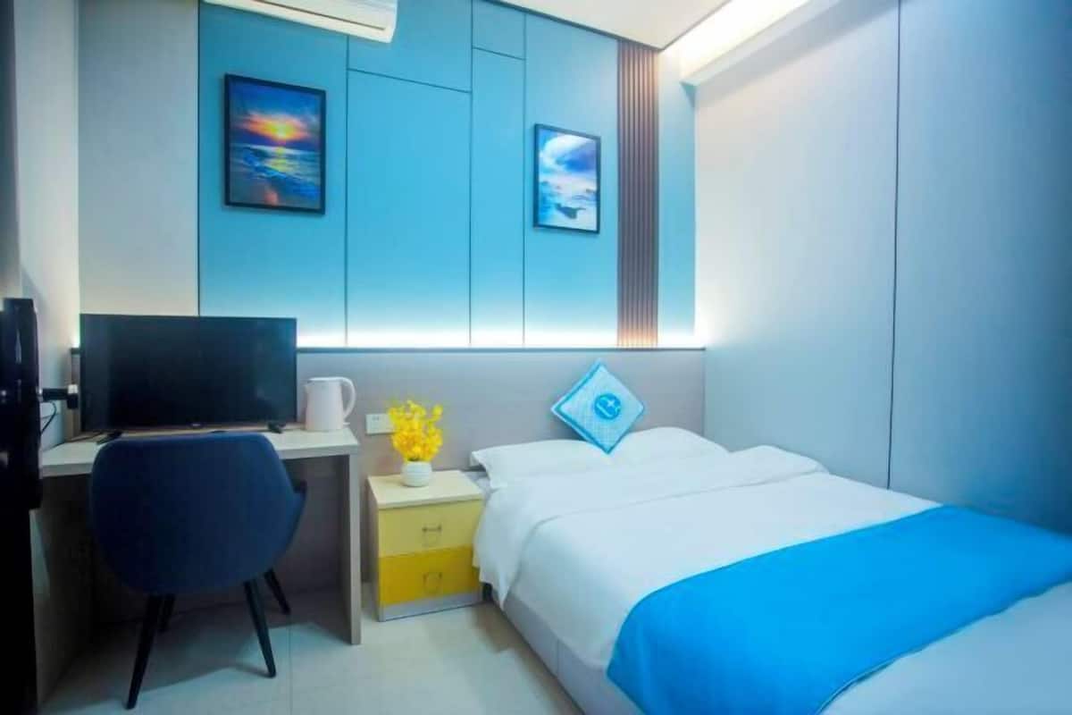 A modern hotel room with a bed, a desk, a chair, and a TV.