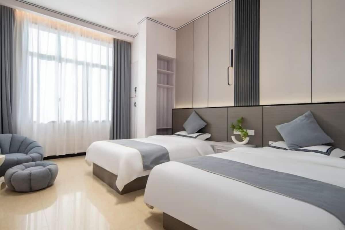 A modern hotel room with two beds, a seating area, and a large window with curtains.