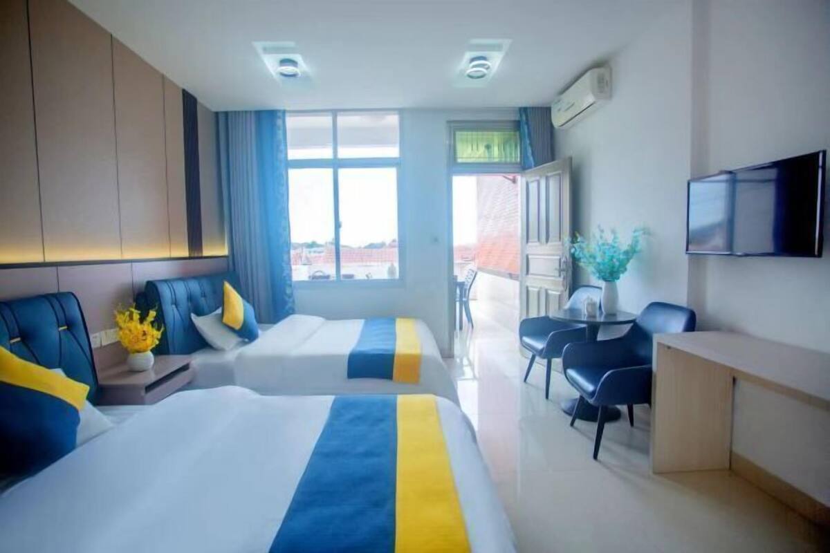 A hotel room with two beds, a desk, a chair, a TV, and a window with a view.