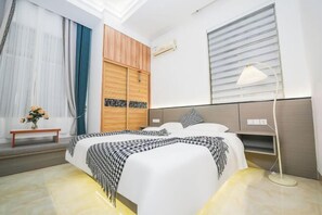 A modern hotel room with a large bed, a bedside lamp, a wooden wardrobe, and a window with blinds. - Chaoyang Hotel (Putian)