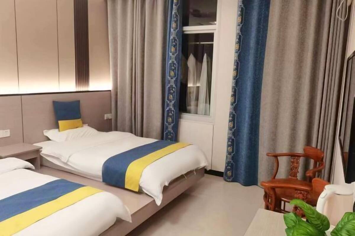 A hotel room with two beds, a wooden chair, a table, and a window with curtains.