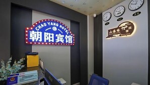 Uma área de recepção de hotel com um letreiro de neon do Hotel Chao Yang, um balcão de recepção, um relógio e um relógio fixado na parede.