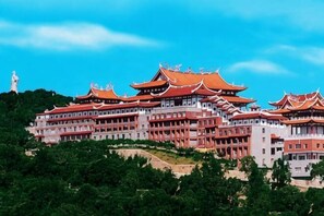 A traditional multi-story building with a series of red-tiled roofs and white walls, surrounded by greenery. - Chaoyang Hotel (Putian)