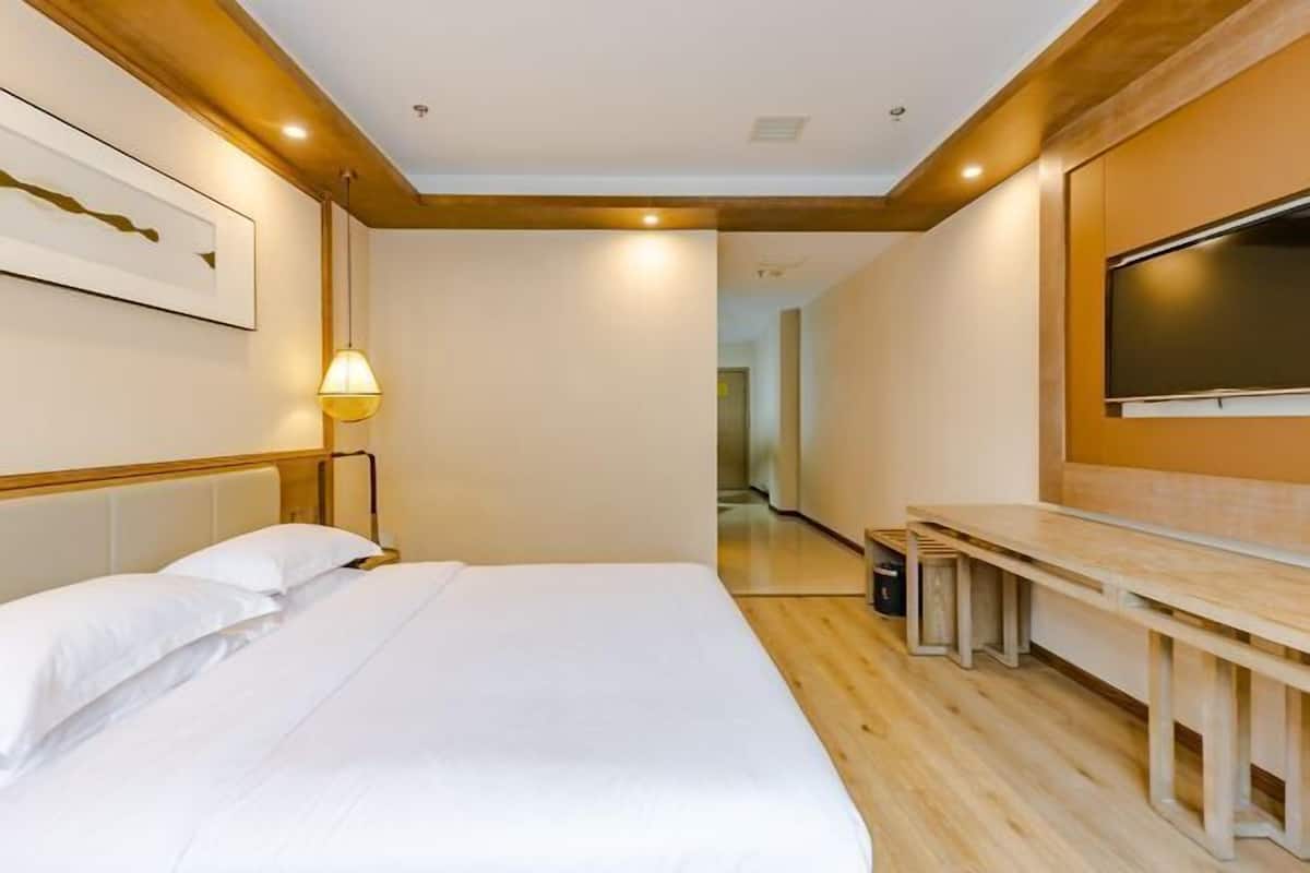 A hotel room with a bed, a TV mounted on the wall, a bench, and a lamp.