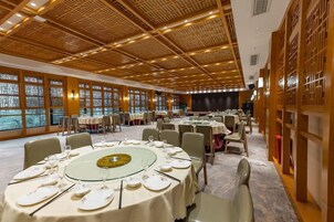 Un salón de banquetes con mesas redondas dispuestas para comer, un escenario y un techo de madera tradicional.
