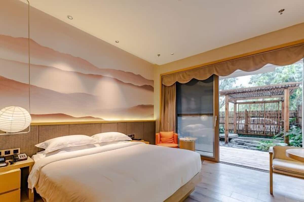 A bedroom with a large bed, a nightstand, a chair, and a view of a wooden deck.
