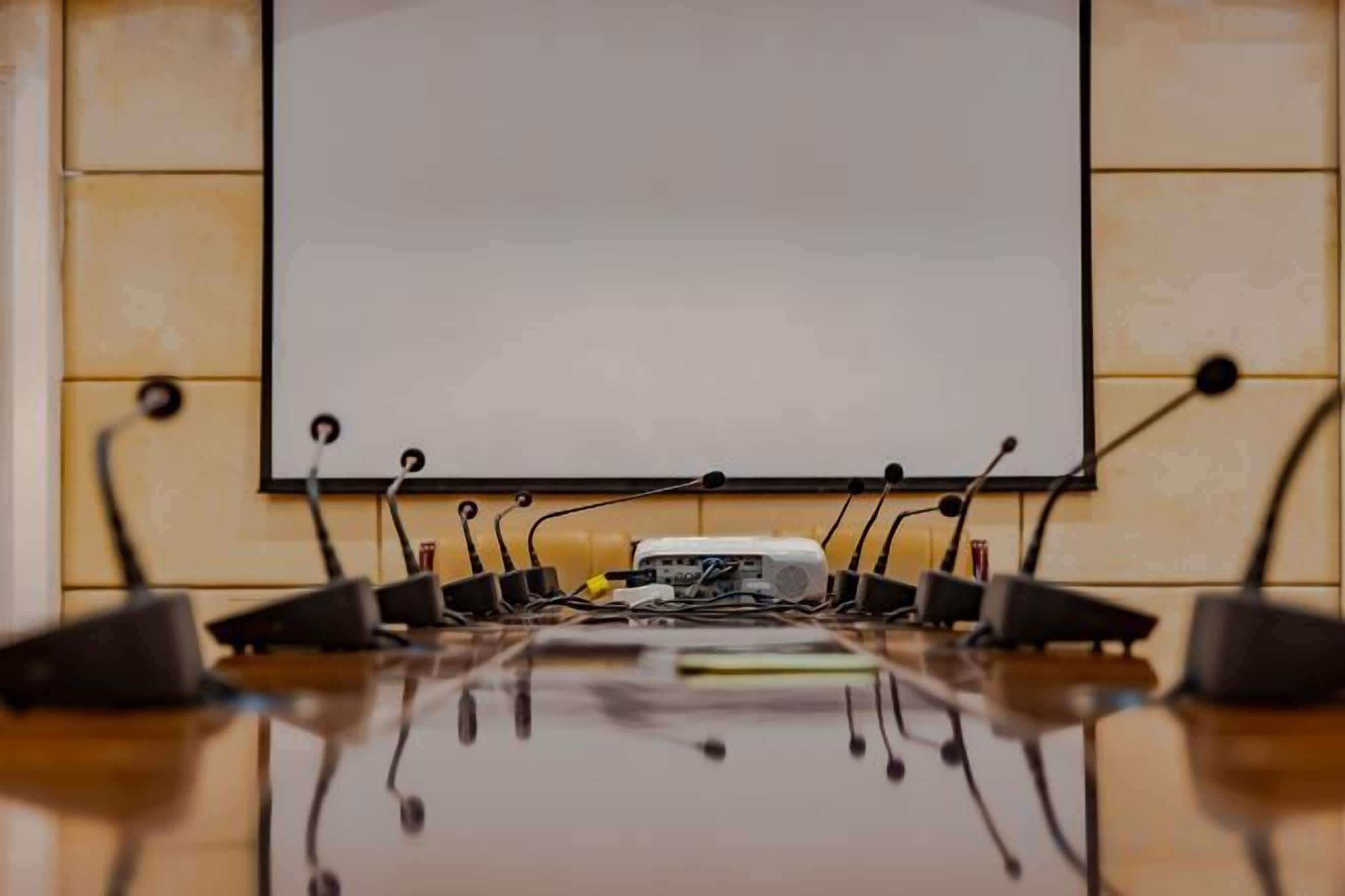 A conference room with a whiteboard, a projector, and multiple microphones on a table.