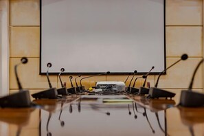 Une salle de conférence équipée d’un tableau blanc, d’un projecteur et de plusieurs microphones placés sur une table.